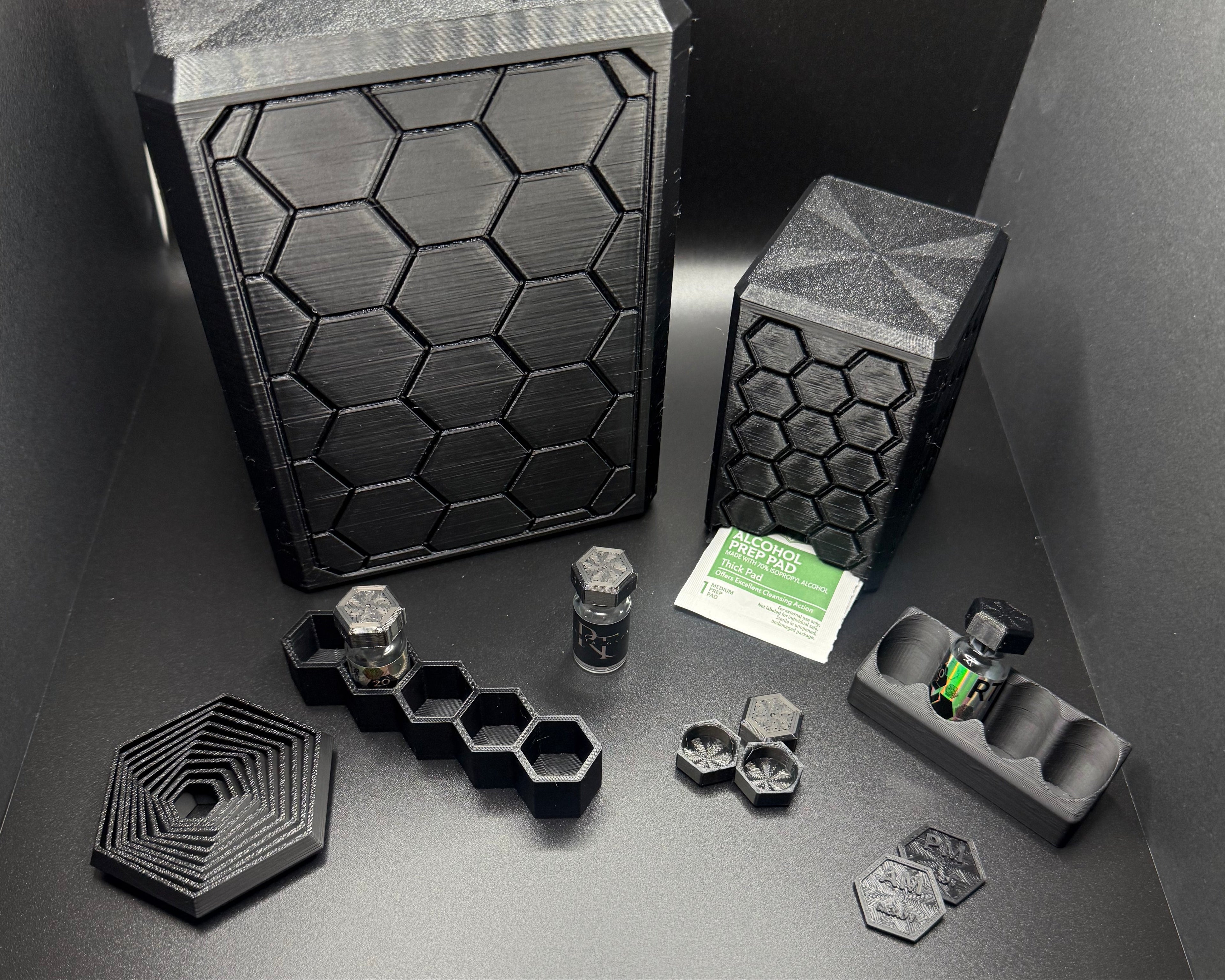 Black Hexagonal wellness station accessories including wipes holder, vial trays and vial caps on a dark surface